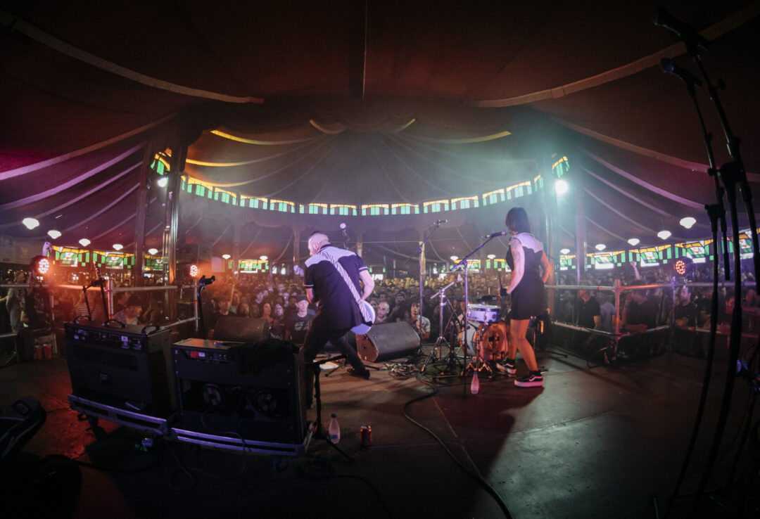 Banda actuando en el escenario de Trashville, el espacio temático del Azkena Rock Festival, con público disfrutando del ambiente íntimo y decorado con vidrieras y luces cálidas.