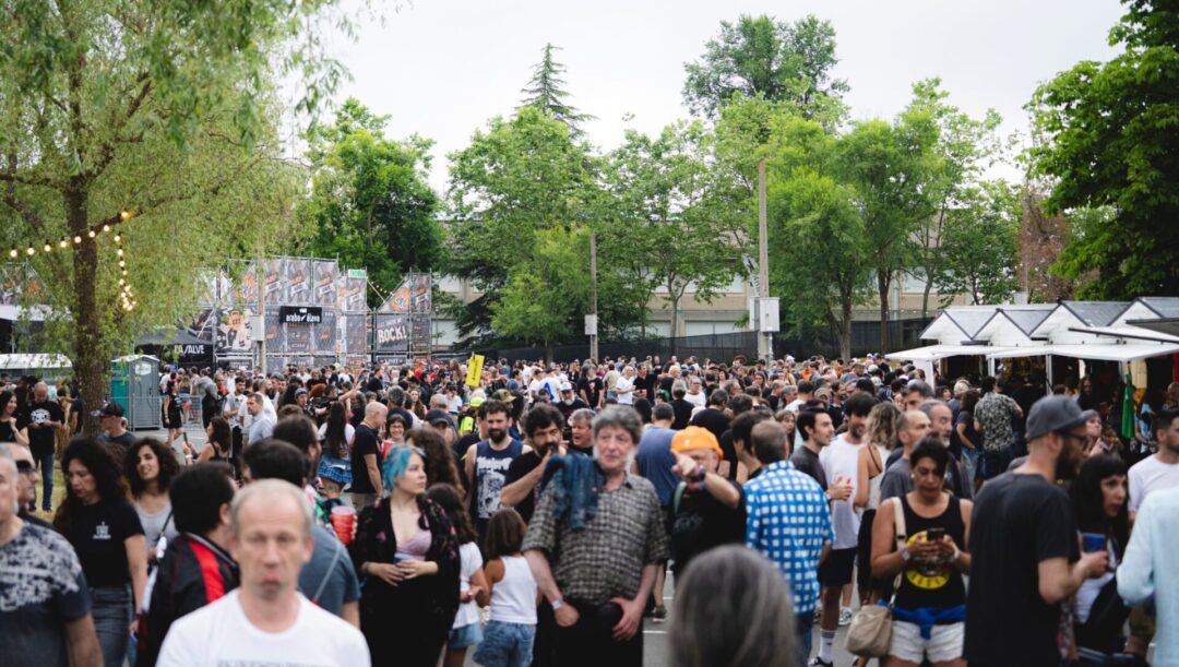 Gran multitud en la zona de acceso del Azkena Rock Festival, entre árboles y puestos, creando ambiente de festival.