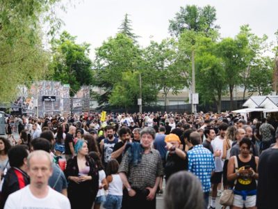 Gran multitud en la zona de acceso del Azkena Rock Festival, entre árboles y puestos, creando ambiente de festival.