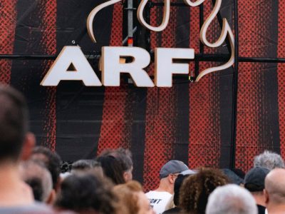 Primer plano del logo “ARF” iluminado sobre un fondo rojo y negro, con público en la parte inferior de la imagen.