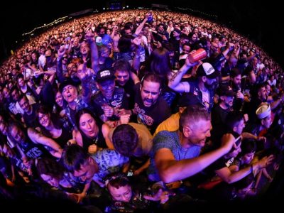 Público del Azkena Rock Festival abarrotando la primera fila de un concierto, cantando y levantando los brazos.