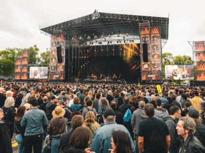 Escenario principal del festival con pantallas gigantes y decoraciones de llamas, rodeado de una multitud disfrutando del concierto.